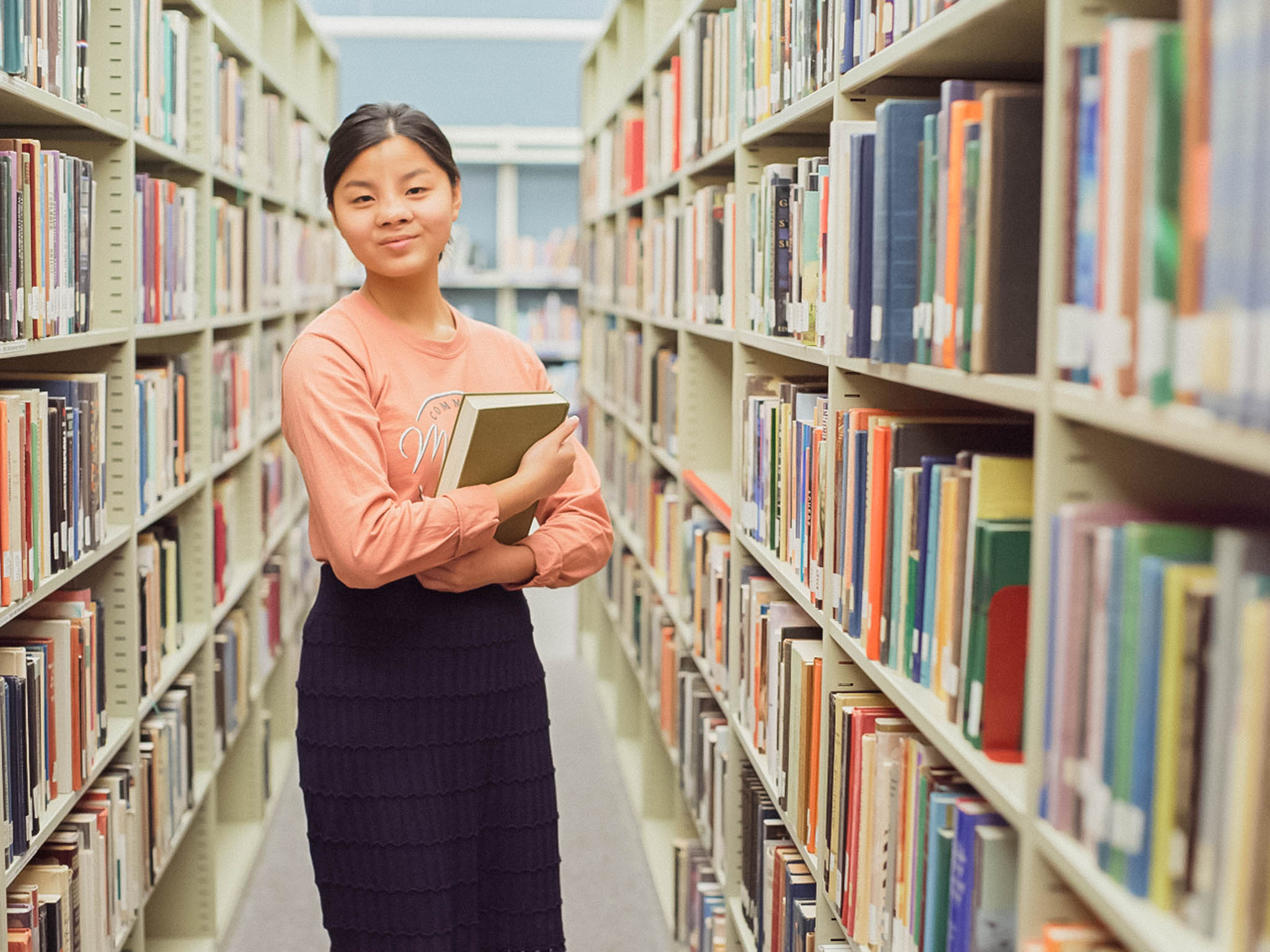 woman holding books in the isle of a library